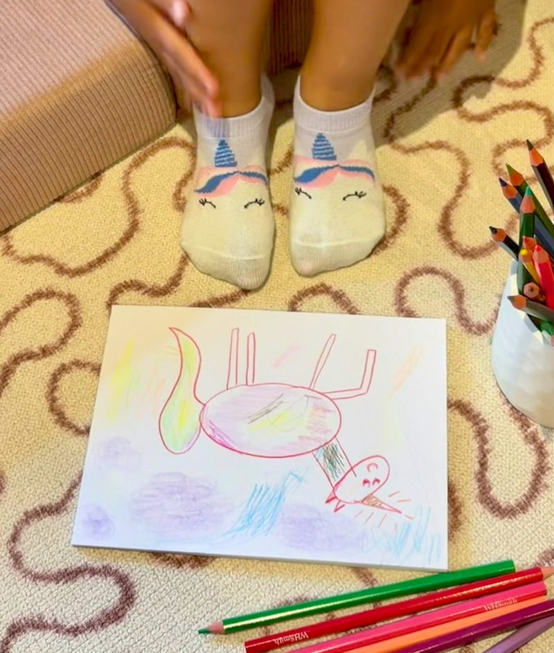 a child in unicorn socks beside her unicorn drawing